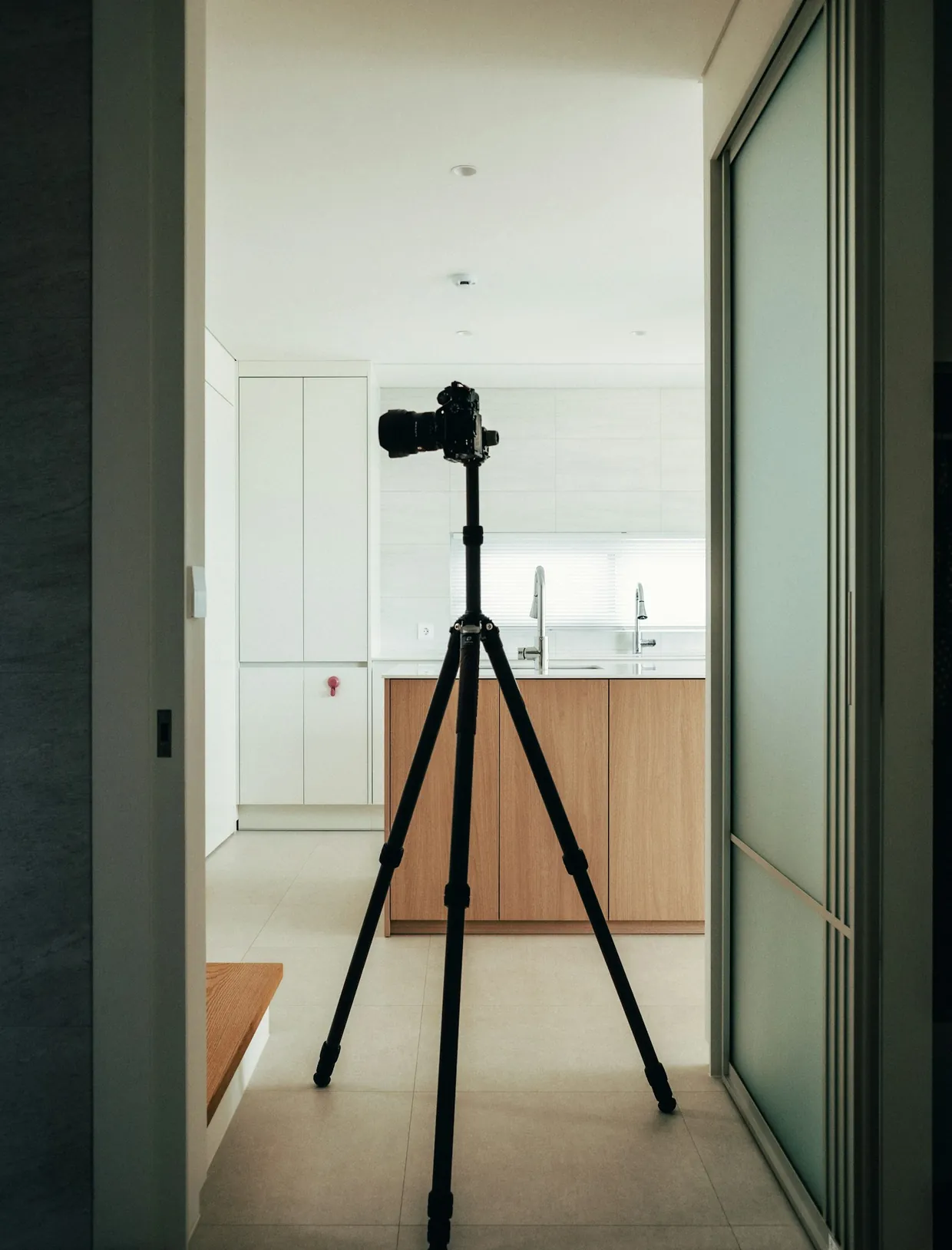 A camera on its tripod in the hallway of a home, pointed at the kitchen